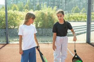 niños y Deportes concepto. retrato de sonriente muchachas posando al aire libre en padel Corte con raquetas y tenis pelotas foto