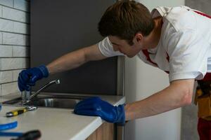 Plumber checking water flow from tap in kitchen, closeup. Repair service photo