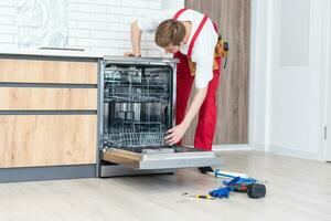 Full length of repairman repairing dishwasher with screwdriver in kitchen. photo