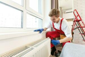 Full length shot of two professional plumbers, workers in uniform fixing or installing heating radiator. Construction, maintenance and repair concept. photo