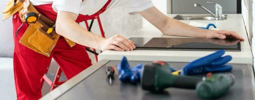 Gloved craftsman installs hob in kitchen. Household Appliance Installation Services Concept photo