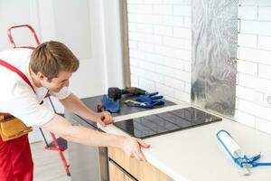 craftsman installs hob in kitchen. Household Appliance Installation Services Concept photo