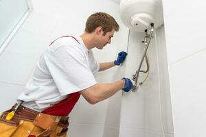 Closeup of plumber using screwdriver while fixing boiler or water heater, working on heating system in apartment photo