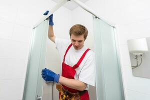 Young man repairing door of shower cabin in bathroom. photo