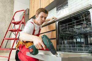 Repairman checks operating state of dishwasher in kitchen photo