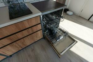 Open clean empty dishwasher in kitchen, closeup photo