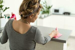 Woman cleaning and polishing the kitchen worktop with a spray detergent, housekeeping and hygiene concept. photo