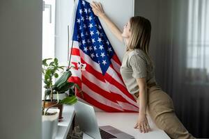 Happy woman employee sitting wrapped in USA flag, shouting for joy in office workplace, celebrating labor day or US Independence day. photo