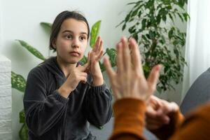 linda pequeño niña hacer mano gesto aprendizaje firmar idioma con mamá o hembra niñera, sonriente pequeño niño práctica no verbal hablar con profesor a hogar, preescolar discapacitado niño tener lección con tutor foto