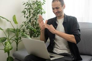 Happy smiling deaf young caucasian man uses sign language while video call using laptop while sitting at home, virtual communication concept. photo