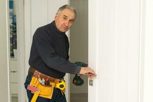 Ordinary elderly man independently repairs a door photo