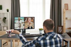 Invalid man in wheelchair greeting people during a video call working from home. Young disabled freelancer doing his business online, using high technology, sitting in his apartment, working remotely in special conditions. photo