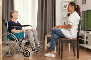 Caregiver talking with a disabled woman sitting in wheelchair. Disabled handicapped old person recovering professional help nurse, nursing retirement home treatment and rehabilitation photo