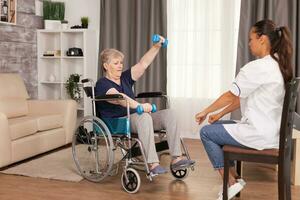 Invalid senior woman using weights with the help of nurse. Disabled handicapped old person recovering professional help nurse, nursing retirement home treatment and rehabilitation photo