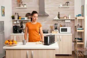 Waiting for the bread to be toasted. Housewife toasting bread slices for delicious breakfast in kitchen. Housewife using bread toaster for delicious breakfast. Healthy morning in cozy interior, delicious home meal preparation photo