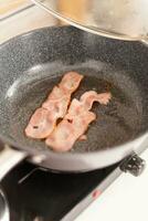 Fried bacon in the pan for a delicios breakfast. Healthy morning in cozy interior, delicious home meal preparation. photo
