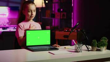 Kid influencer in home studio using recording gear to record review of mockup laptop. Young girl online show host filming electronics haul, presenting isolated screen notebook for viewers video