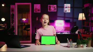 Smiling child in home studio presenting advertisement from sponsoring brand on green screen tablet. Little kid using chroma key device to present promotion from media partner to followers video