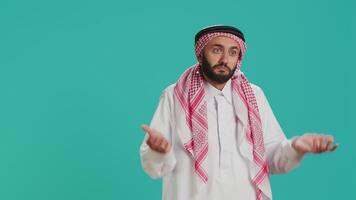 Muslim person being confused and unsure on camera, creating i dont know symbol and acting clueless over blue background. Young man in arab clothing being uncertain and shrugging. video