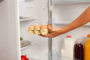 Woman taking out eggs from fridge in the morning for breakfast. Housewife getting helthy eggs and other ingredients from refrigerator in her kitchen. photo