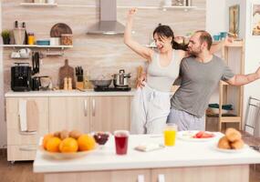 emocionado contento Pareja bailando en cocina vistiendo pijama durante desayuno. despreocupado esposa y marido riendo teniendo divertido gracioso disfrutando vida auténtico casado personas positivo contento relación foto