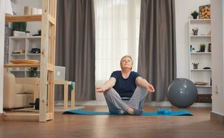 Senior woman relaxing in living room doing yoga. Active healthy lifestyle sporty old person training workout home wellness and indoor exercising photo