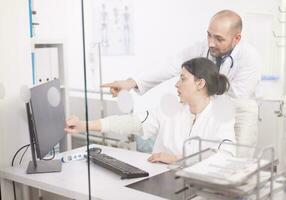 Team of doctors pointing at computer in hospital room wearing white coat and stethoscope. Medical colleagues. photo