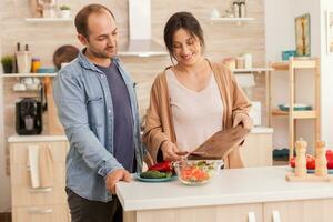 Couple making salad together in kitchen. Sliced vegetables. Happy in love cheerful and carefree couple helping each other to prepare meal photo