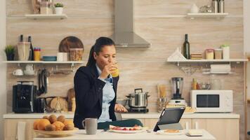 Businesswoman drinking fresh juice during breakfast before work watching a video on tablet. Business woman reading the last news online before going to work, using modern technology in the kitchen while eating a healthy meal photo
