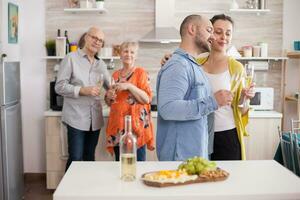 Happy couple with wine glasses in kitchen having a conversation. Appetizer with assorted cheese. Bottle of wine on table top. photo