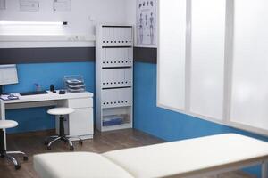 The image showcases a clinic office that is used for consultations and appointments. An empty hospital room containing a desk with a computer for a doctor and an examination bed. photo