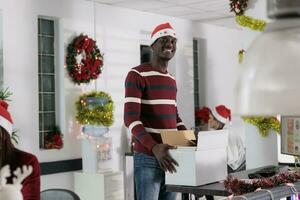 retrato de alegre africano americano empleado contento a comienzo nuevo trabajo en Navidad decorado oficina. sonriente trabajador contratado para nuevo empresa posición apertura durante festivo fiesta temporada foto