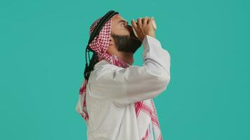 Islamic person drinking cup of coffee in the morning, enjoying refreshment with caffeine for vitality and energy. Middle eastern man with robe and headscarf serving hot drink. video