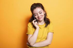 en estudio, caucásico mujer usos su teléfono inteligente a hacer un teléfono llamada a amigos. sonriente morena dama utilizando moderno tecnología con móvil dispositivo para remoto teléfono comunicación. foto