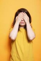 Troubled woman covering face and eyes with palms. Female person standing with hands on closed eyes, feeling emotional over isolated background. Shy person hiding facial expression from camera. photo