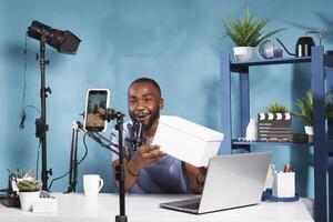 Man blogger announcing giveaway while streaming on social media network channel using smartphone. Vlogger showing gift box to subscribers and looking at mobile phone camera photo