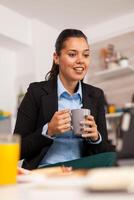 mujer de negocios teniendo un bueno día con genial noticias. persona de libre dedicación leyendo el último Noticias en línea antes de yendo a trabajar, utilizando moderno tecnología en el cocina mientras comiendo un sano comida foto