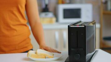 Woman waiting for roasted bread to pop from electric toaster. Housewife using bread toaster for delicious breakfast. Healthy morning in cozy interior, delicious home meal preparation photo