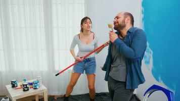 Married couple singing on renovation tools dipped in blue paint. Cheerful married couple during home makeover. Home decoration and renovation in cozy apartment flat, repair and makeover photo