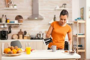 mujer torrencial caliente café en taza en el Mañana desde maceta. ama de casa a hogar haciendo Fresco suelo café en cocina para desayuno, Bebiendo, molienda café Café exprés antes de yendo a trabajo foto