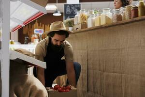 Farmer bringing crates full of vegetables from his own renewable energy powered farm to zero waste supermarket. Supplier restocks local neighborhood store with sustainable handpicked food items photo