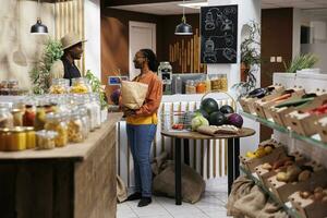 African American shopkeeper and customer discuss eco friendly, pantry staples and fresh produce. Sustainable shopping, bulk items, and plasticfree standards. Focus on background. photo