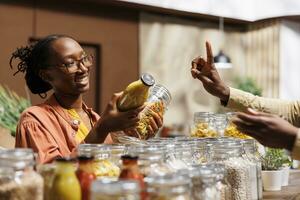 en almacenar, un africano americano vendedor ofertas orgánico, regionalmente producido alimento. Fresco vegetales y despensa esenciales sin el plastico son dado a hembra cliente por el tendero. de cerca fotografía. foto