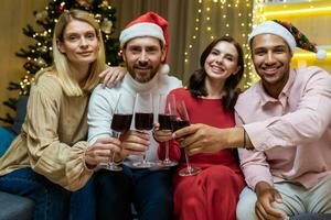 Portrait of a group of diverse guests at home for the new year, friends celebrating Christmas looking at the camera and smiling holding glasses of wine, sitting on the sofa in the living room cinema. photo