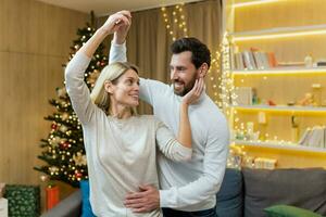 Christmas family couple, man and woman celebrating new year near tree at home, lovers dancing and having fun smiling and hugging. photo