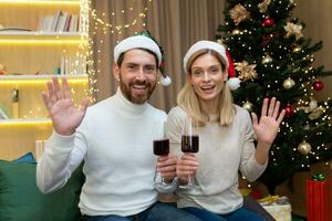 maduro casado Pareja hombre y mujer celebrando Navidad y nuevo año juntos, mirando a web cámara y sonriente hablando a amigos en vídeo llamada participación vino lentes en manos ondulación saludo hogar foto