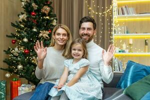 family parents and little girl kid child greeting remotely video conferencing chat call online talk congratulations Merry Christmas Happy New Year, winter holidays looks at camera ,webcam view. photo