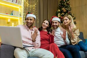 diverso amigos celebrando nuevo año y Navidad juntos hogar, Navidad fiesta con huéspedes, hombres y mujer sonriente y contento juntos hablando en vídeo llamada saludo amigos de forma remota, utilizando ordenador portátil. foto