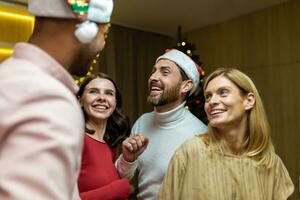 Four diverse friends at New Year's party celebrating and dancing, house guests having fun at Christmas, in New Year's festive clothes and Santa hats in the living room. photo