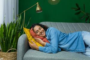 Young beautiful hispanic woman sleeping on sofa at home, woman resting during daytime in living room. photo